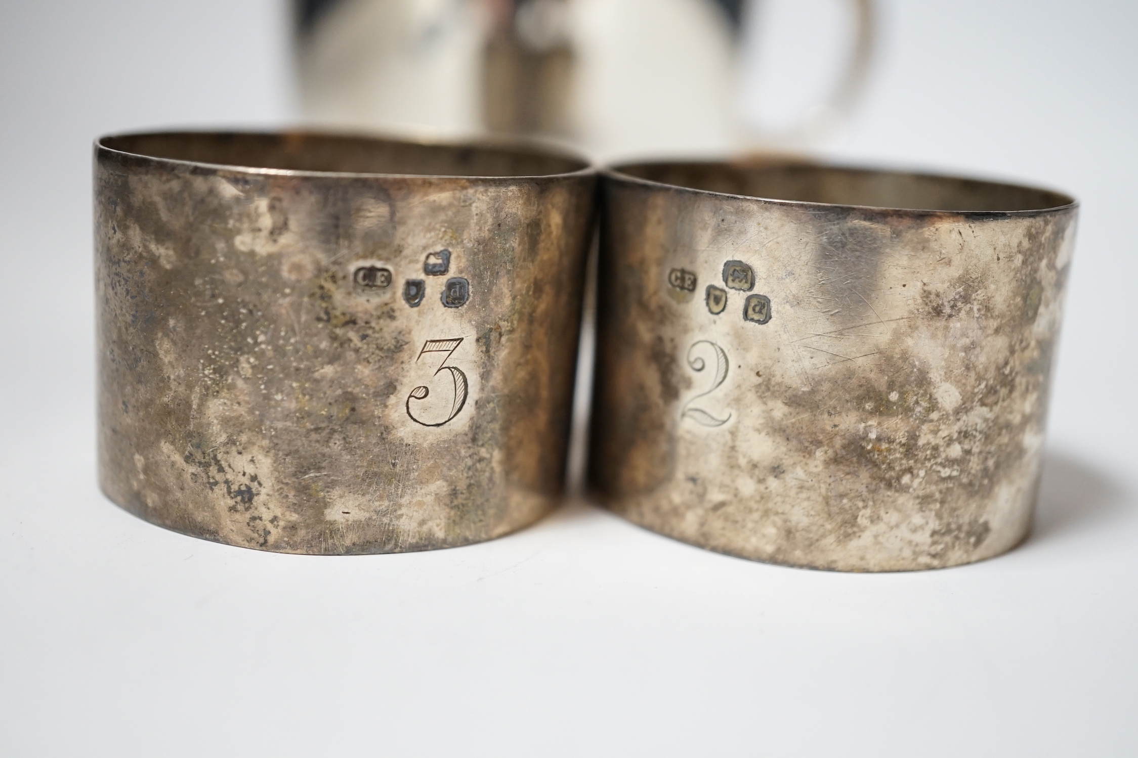 A George V silver cup, with single handle, Searle & Co, London, 1932, height 61mm, together with a pair of late Victorian silver napkin rings, Charles Edwards, London, 1899, 8oz.